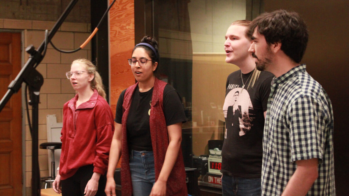 Four adults singing in a choir standing behind microphones