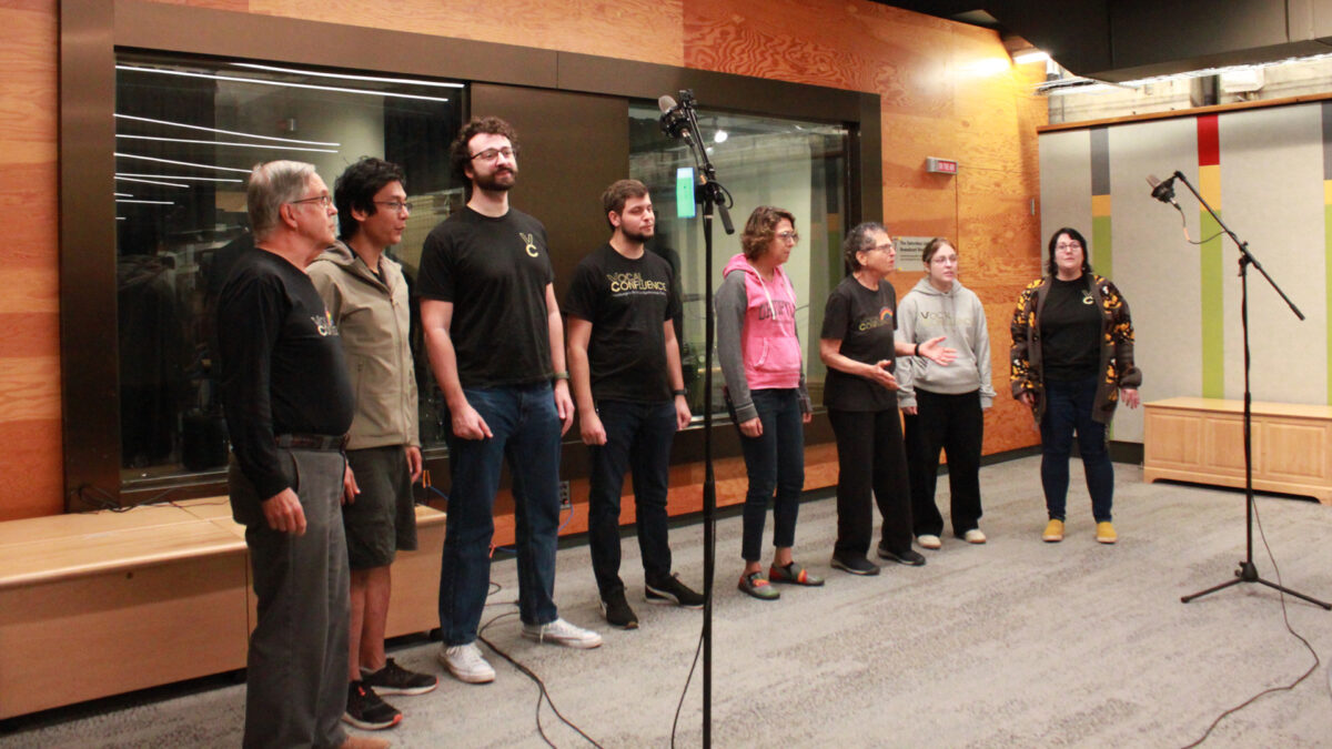 Eight adults singing in a choir standing behind microphones