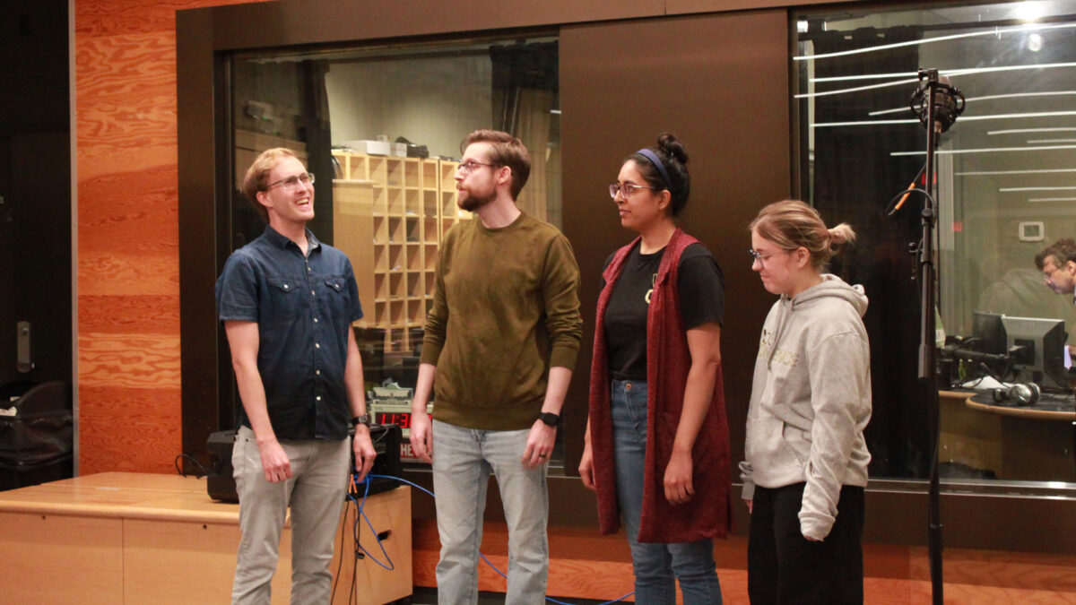 Four adults singing in a choir standing behind microphones