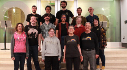 Fourteen adults smiling at the camera and standing on a staircase