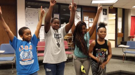 Four youth holding their arms up celebrating in a classroom