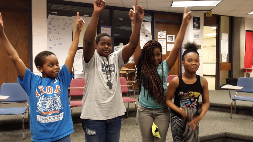 Four youth holding their arms up celebrating in a classroom