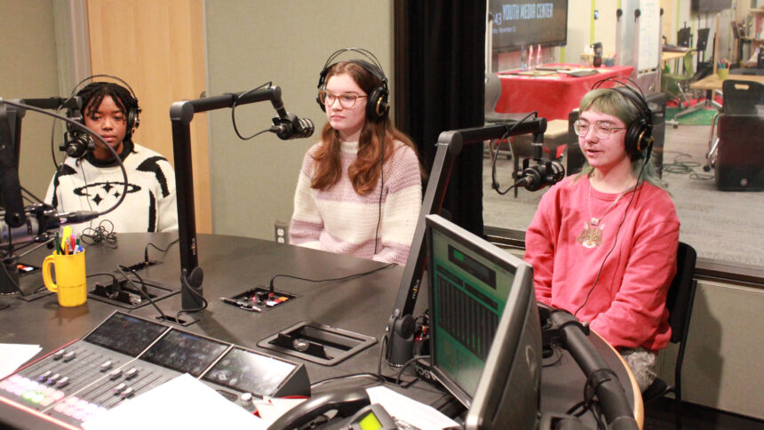 Three teens wearing headphones speaking into microphones in a radio studio