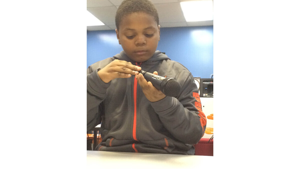 A youth interacting with the bottom of a microphone in a classroom