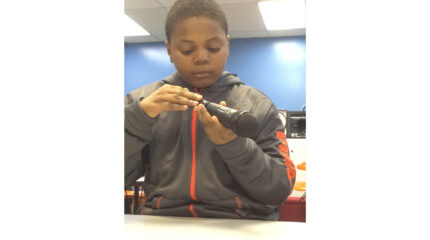 A youth interacting with the bottom of a microphone in a classroom