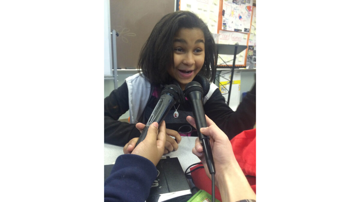 A youth speaking into two held microphone in a classroom