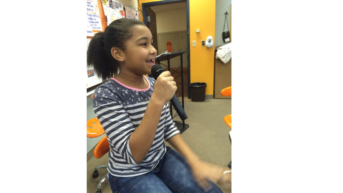 A youth holding and speaking into a microphone in a classroom