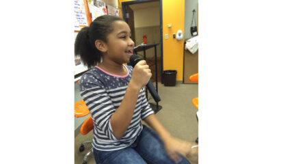 A youth holding and speaking into a microphone in a classroom