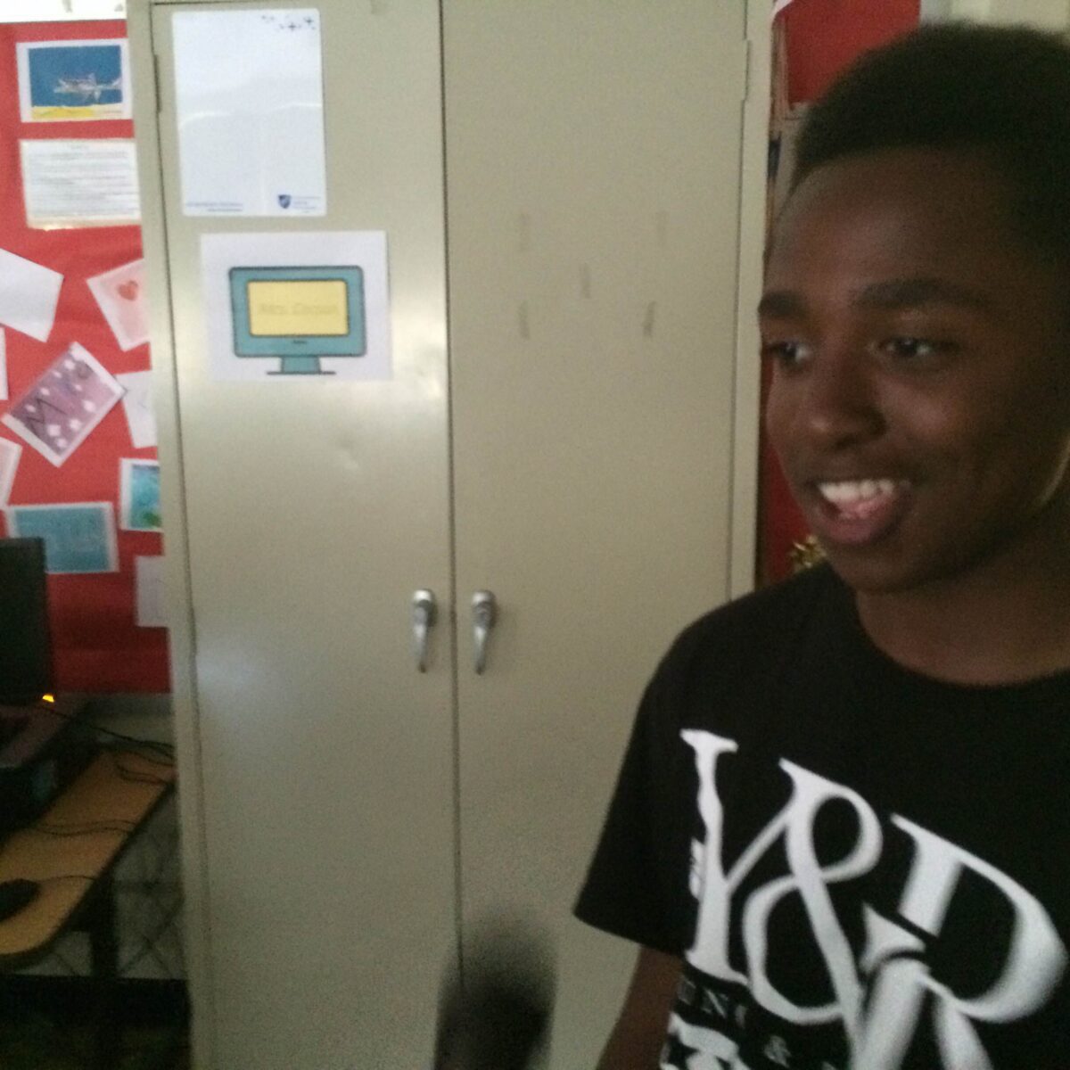 IMG_1056 A youth smiling and standing in front of a gray cabinet