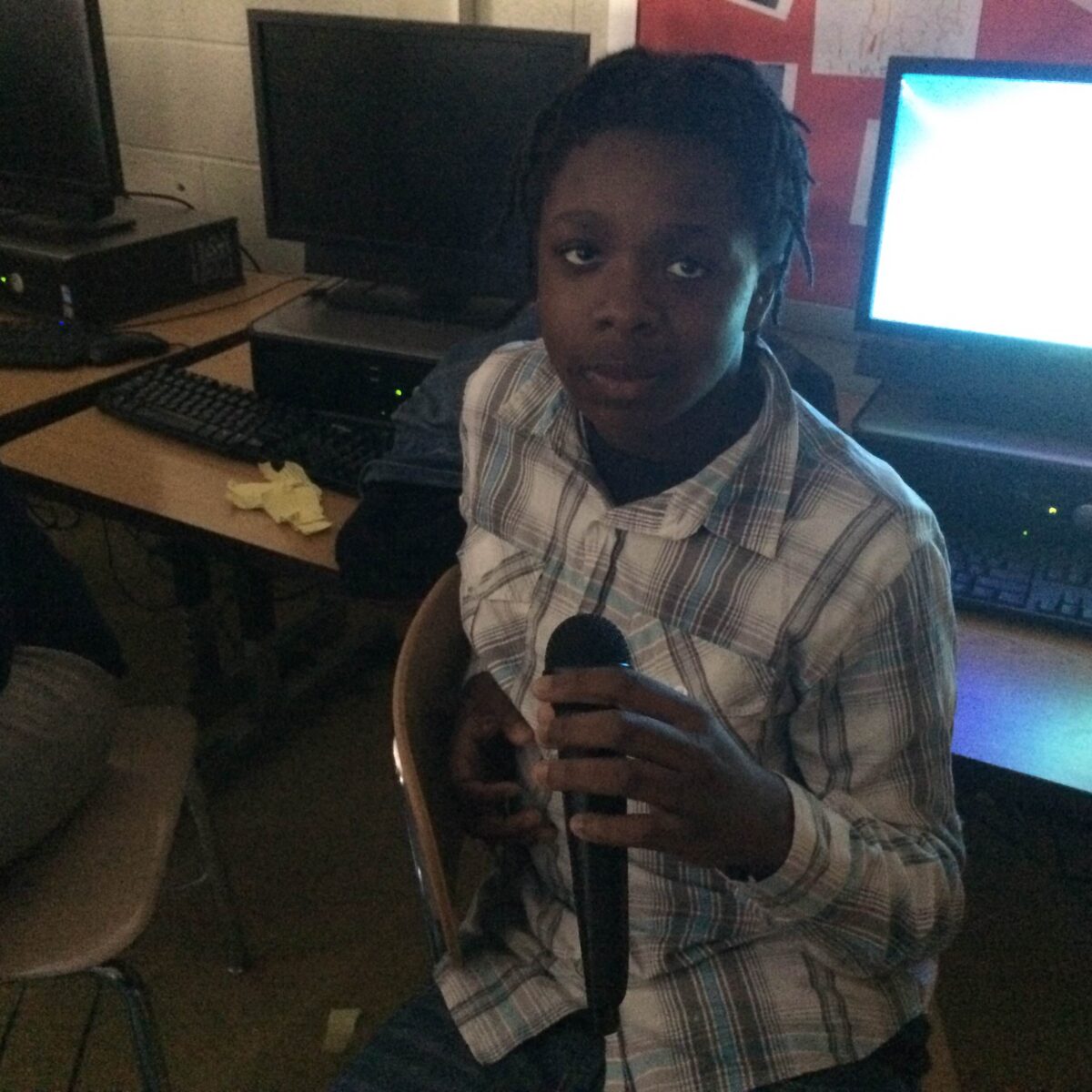 IMG_1060 A youth holding a microphone sitting in front of computers on classroom desks