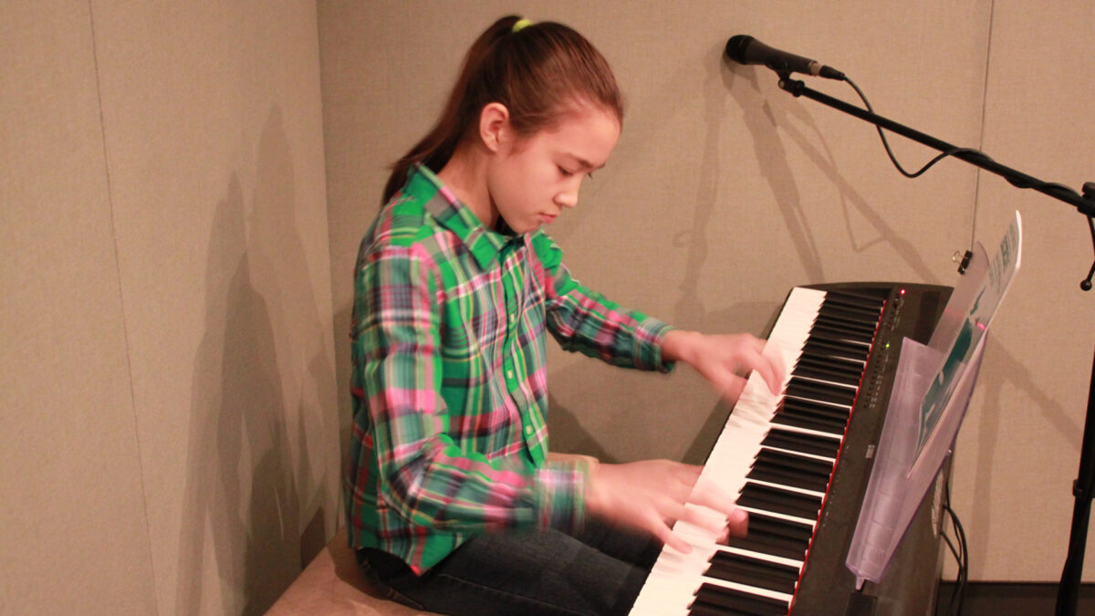 A youth playing a piano keyboard sitting behind a microphone in a radio studio