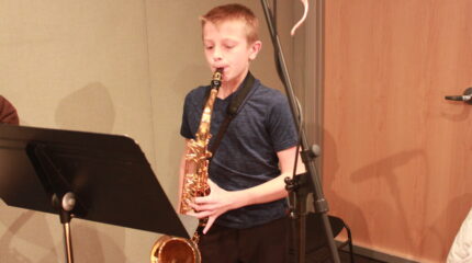 A youth playing saxophone looking at sheet music on a music stand in a radio studio