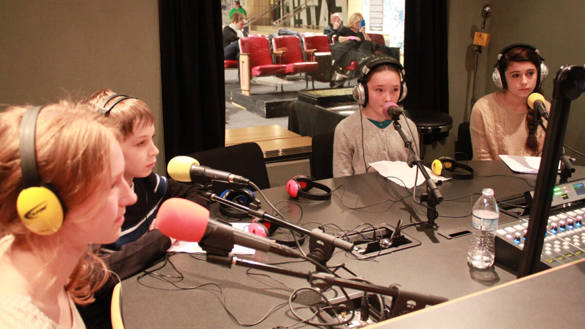 Four youth wearing headphones speaking into microphones in a radio studio