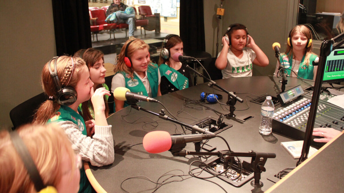 Seven youth wearing headphones speaking into microphones in a radio studio