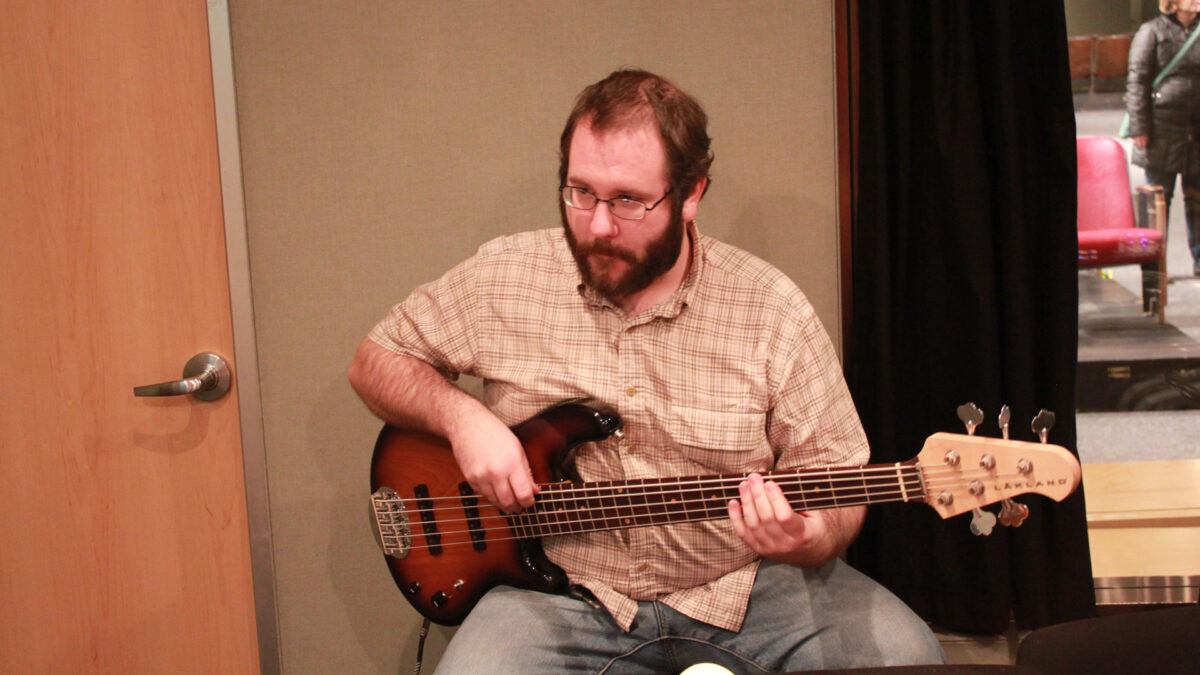 An adult playing an electric bass in a radio studio