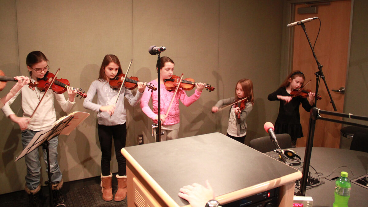 Five youth playing violins in a radio studio