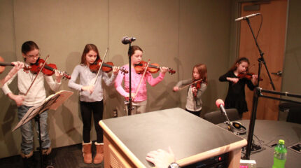 Five youth playing violins in a radio studio