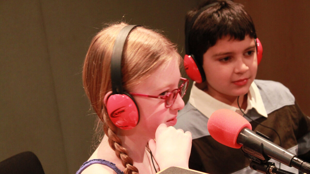 Two youth wearing headphones speaking into microphones in a radio studio