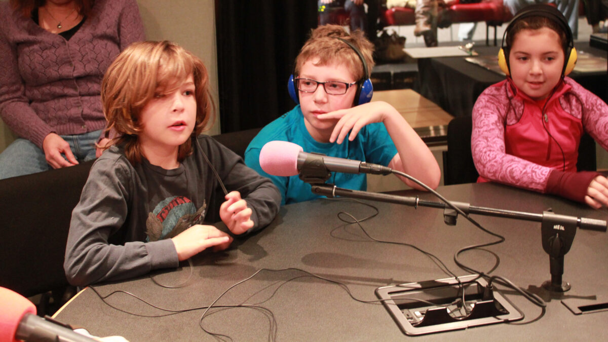 Three youth, two wearing headphones, speaking into microphones in a radio studio
