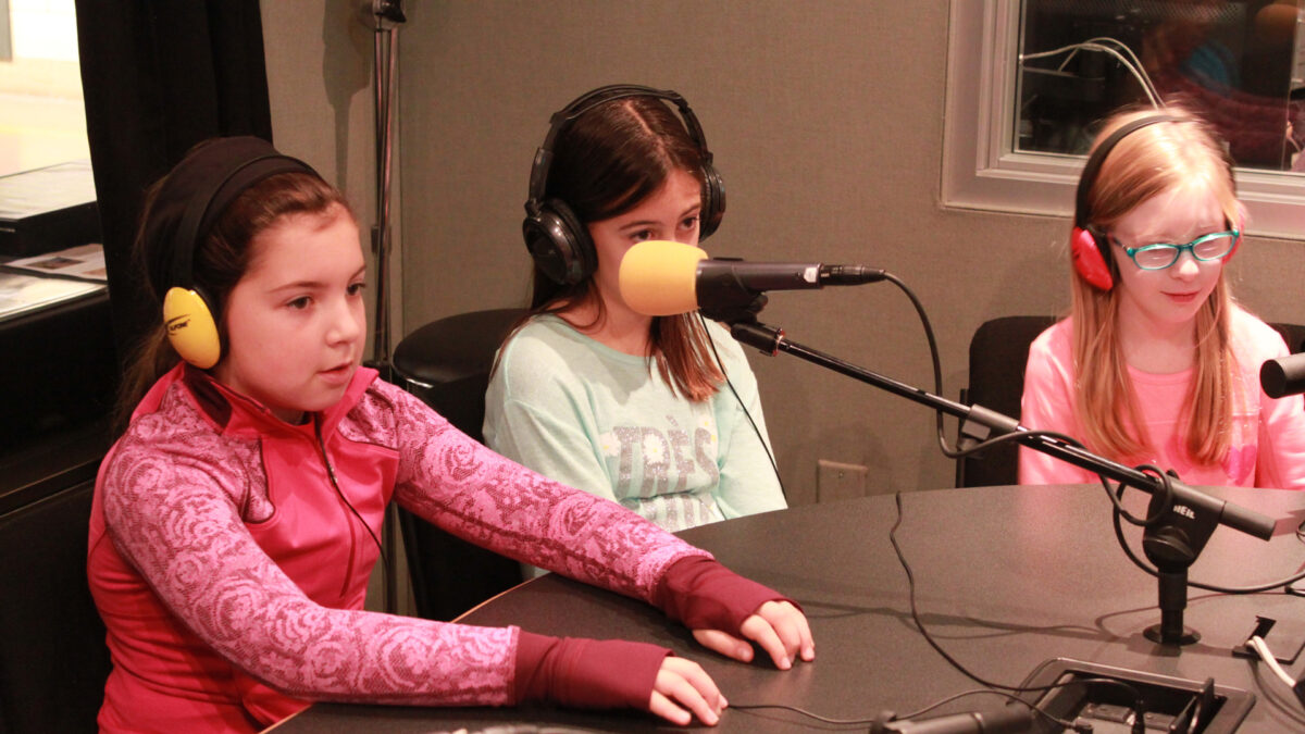 Three youth wearing headphones speaking into microphones in a radio studio