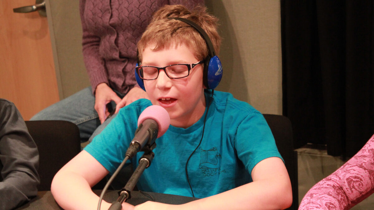 A youth wearing headphones speaking into a microphone in a radio studio