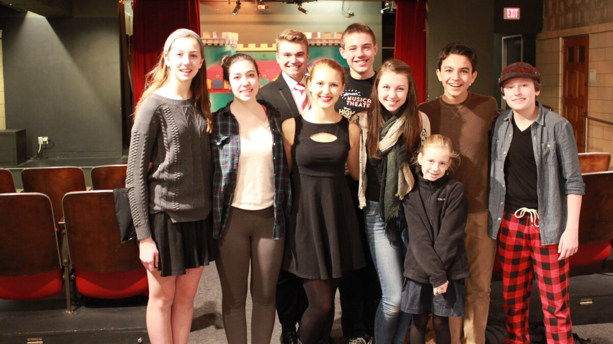 Nine youth smiling and posing in front of an auditorium