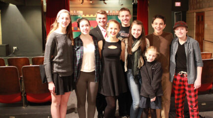 Nine youth smiling and posing in front of an auditorium