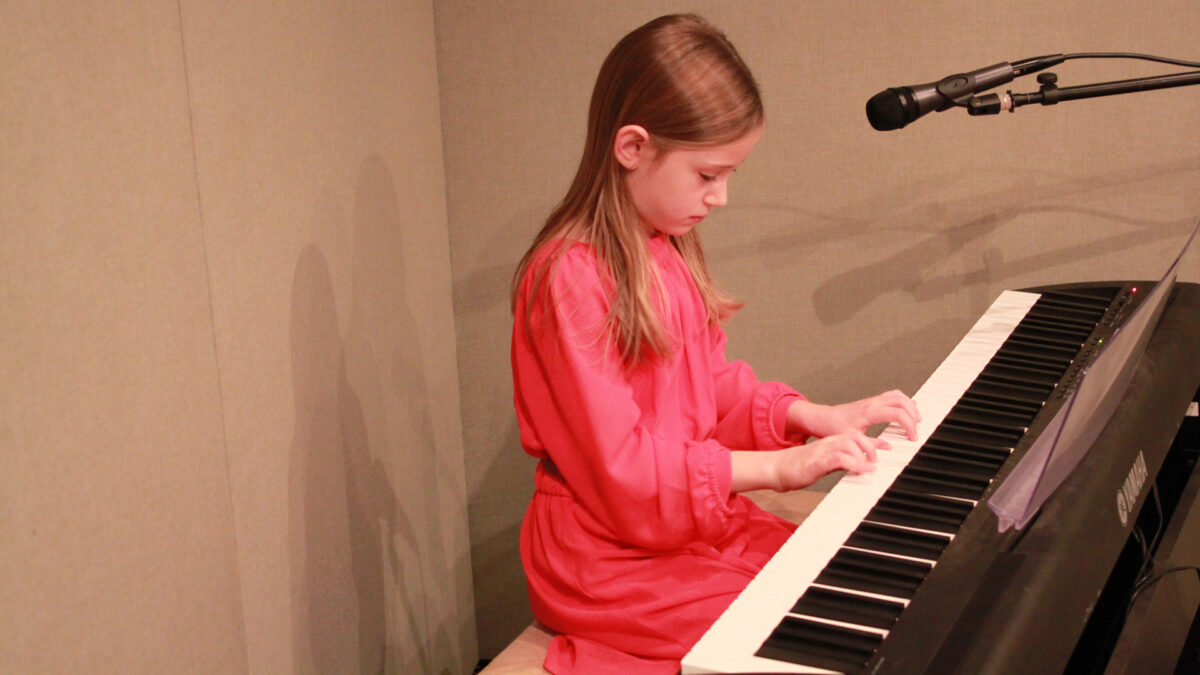 A youth playing a piano keyboard sitting behind a microphone in a radio studio