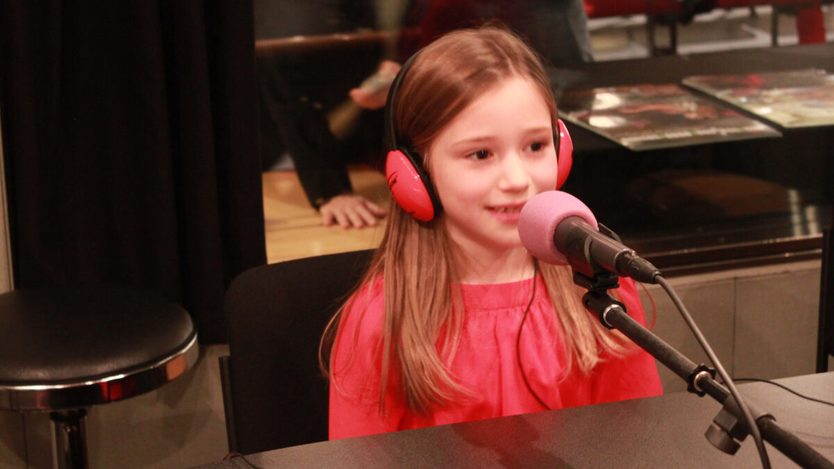A youth wearing headphones speaking into a microphone in a radio studio.