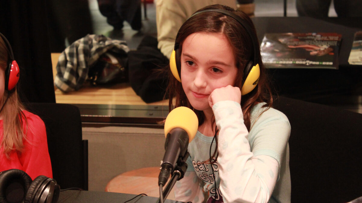A youth wearing headphones sitting behind a microphone in a radio studio