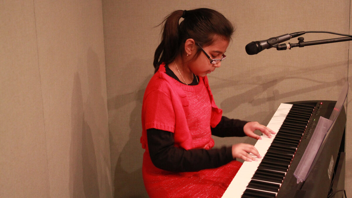 A youth playing a piano keyboard sitting behind a microphone in a radio studio