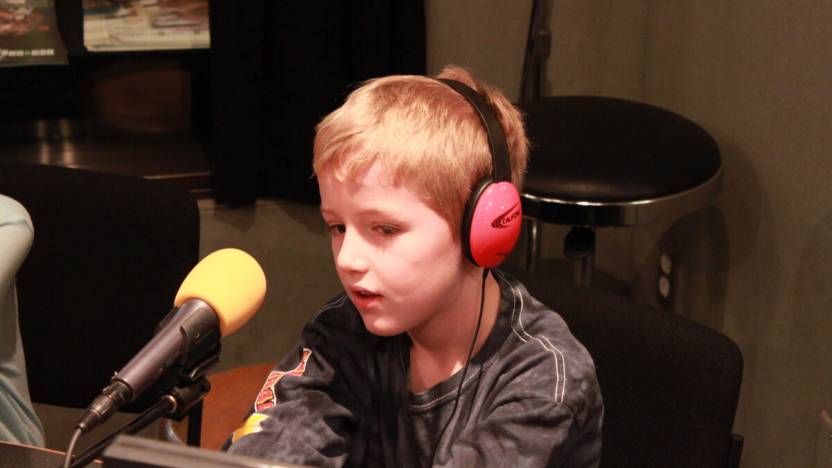 A youth wearing headphones speaking into a microphone in a radio studio