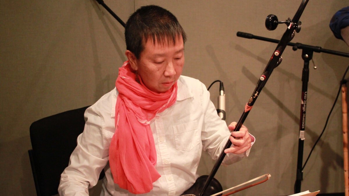 An adult playing an oriental stringed instrument in a radio studio