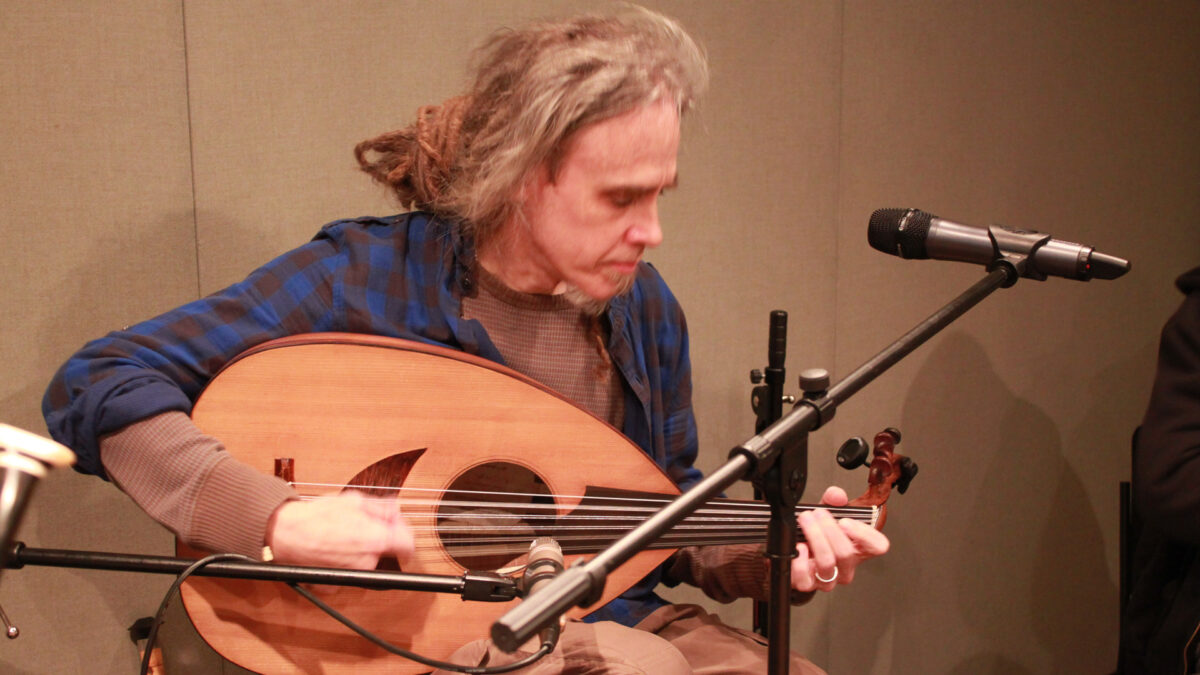 An adult playing a stringed instrument in a radio studio