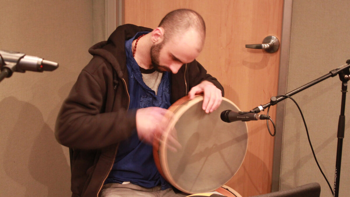 An adult playing a percussion instrument into a microphone in a radio studio