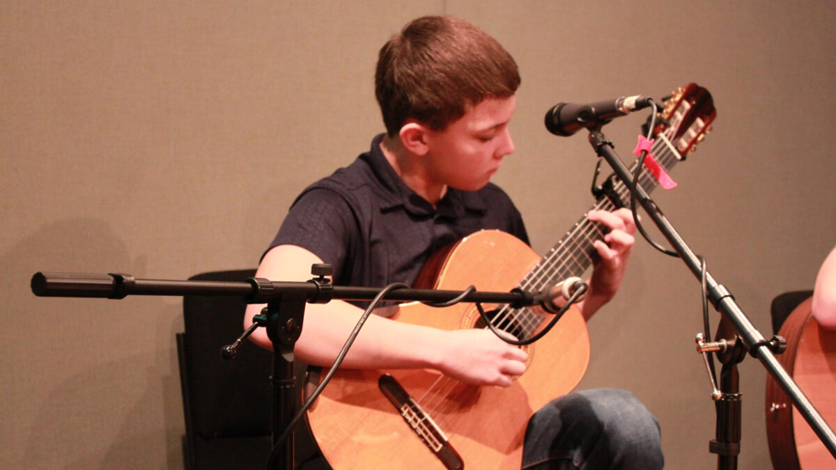 A teen playing an acoustic guitar in a radio studio