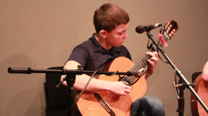 A teen playing an acoustic guitar in a radio studio