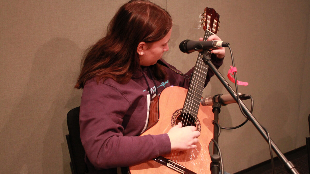A teen playing an acoustic guitar in a radio studio