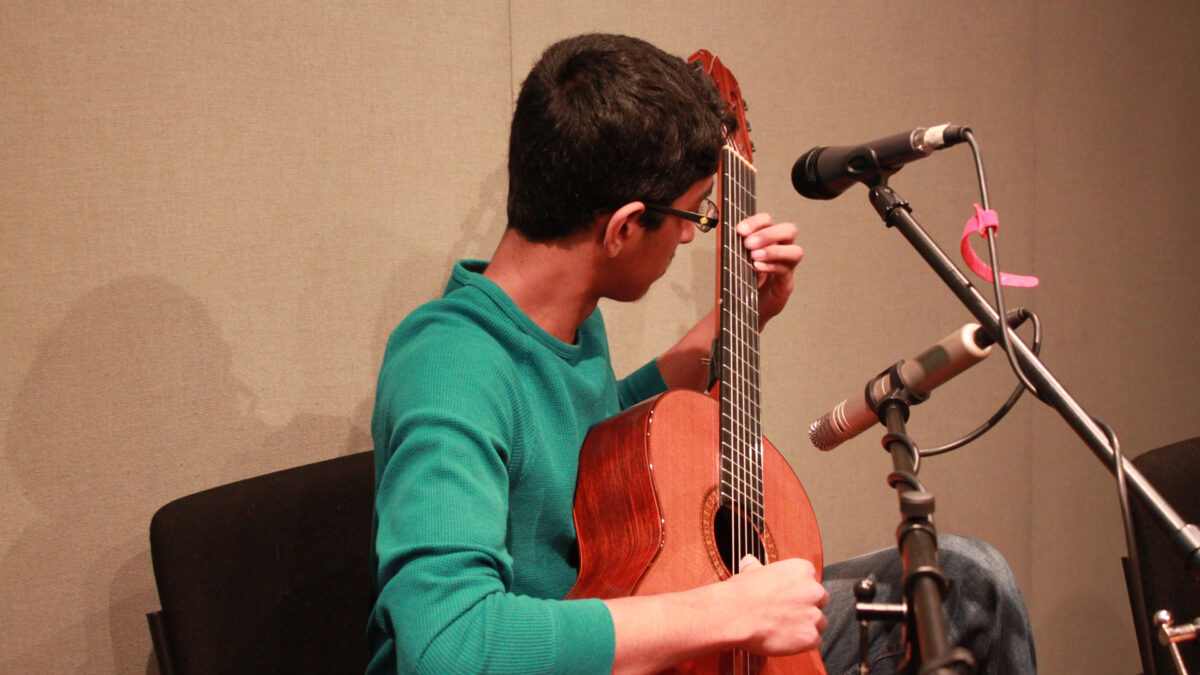 A teen playing an acoustic guitar in a radio studio