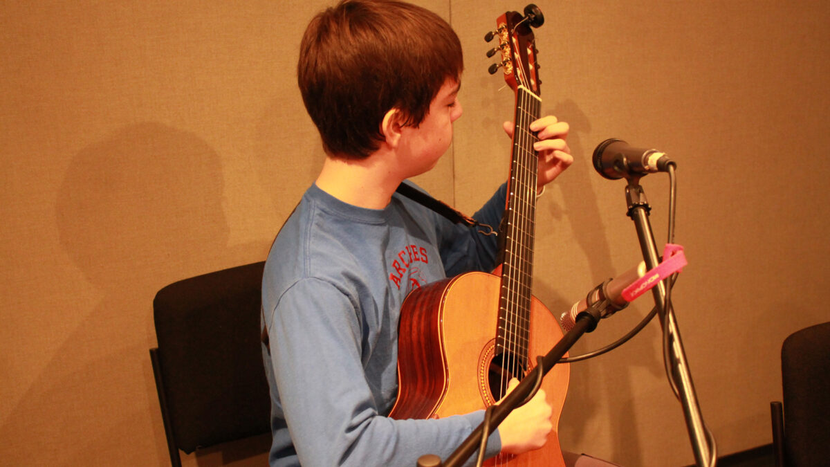A youth playing acoustic guitar in a radio studio
