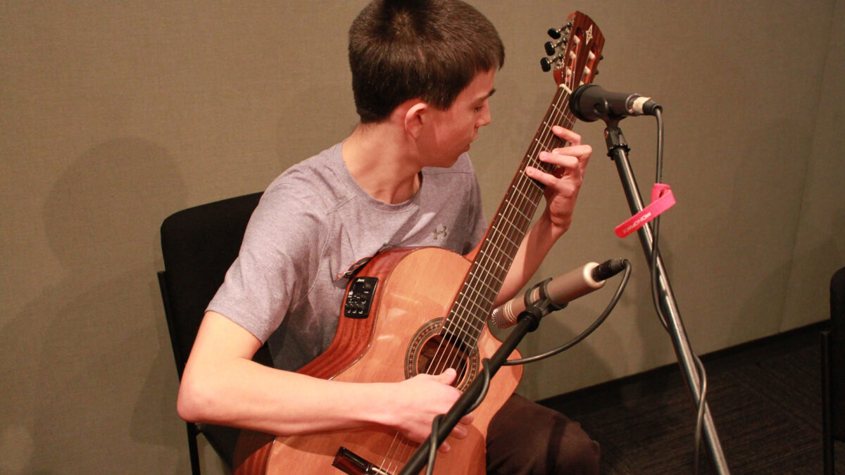 A teen playing acoustic guitar in a radio studio