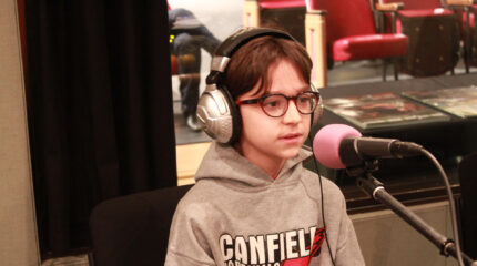 A youth wearing headphones speaking into a microphone in a radio studio