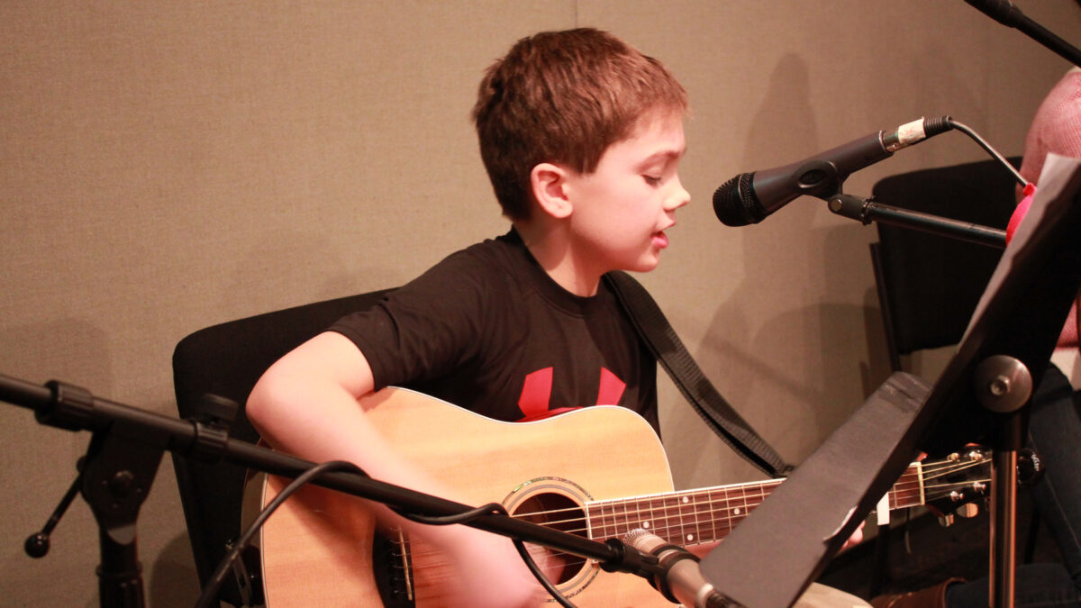 A youth playing acoustic guitar and singing into a microphone in a radio studio