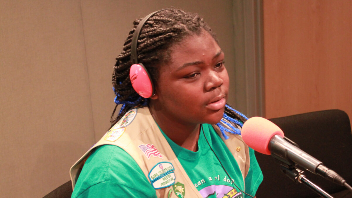 A teen wearing headphones speaking into a microphone in a radio studio