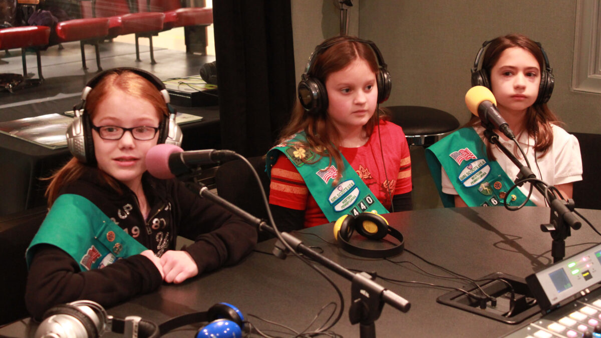 Three youth wearing headphones speaking into microphones in a radio studio