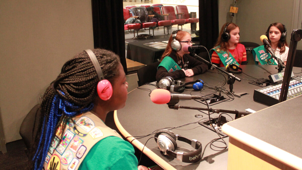 Three youth wearing headphones speaking into microphones in a radio studio