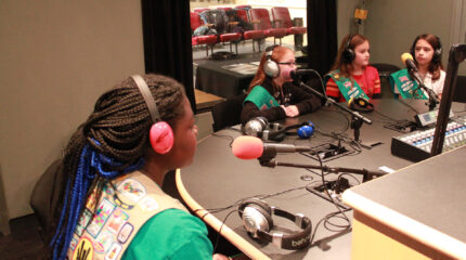Three youth wearing headphones speaking into microphones in a radio studio