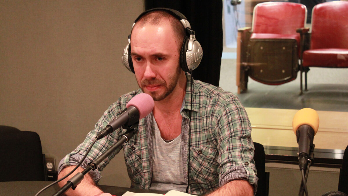 An adult wearing headphones sitting behind a microphone in a radio studio