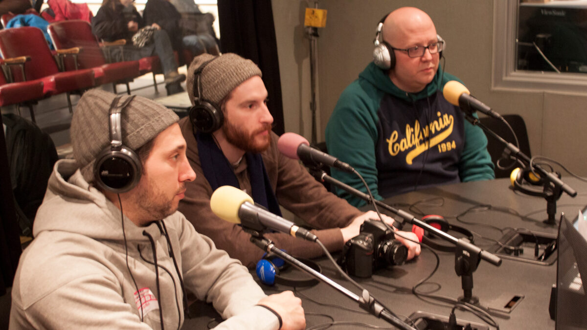 Three adults wearing headphones speaking into microphones in a radio studio