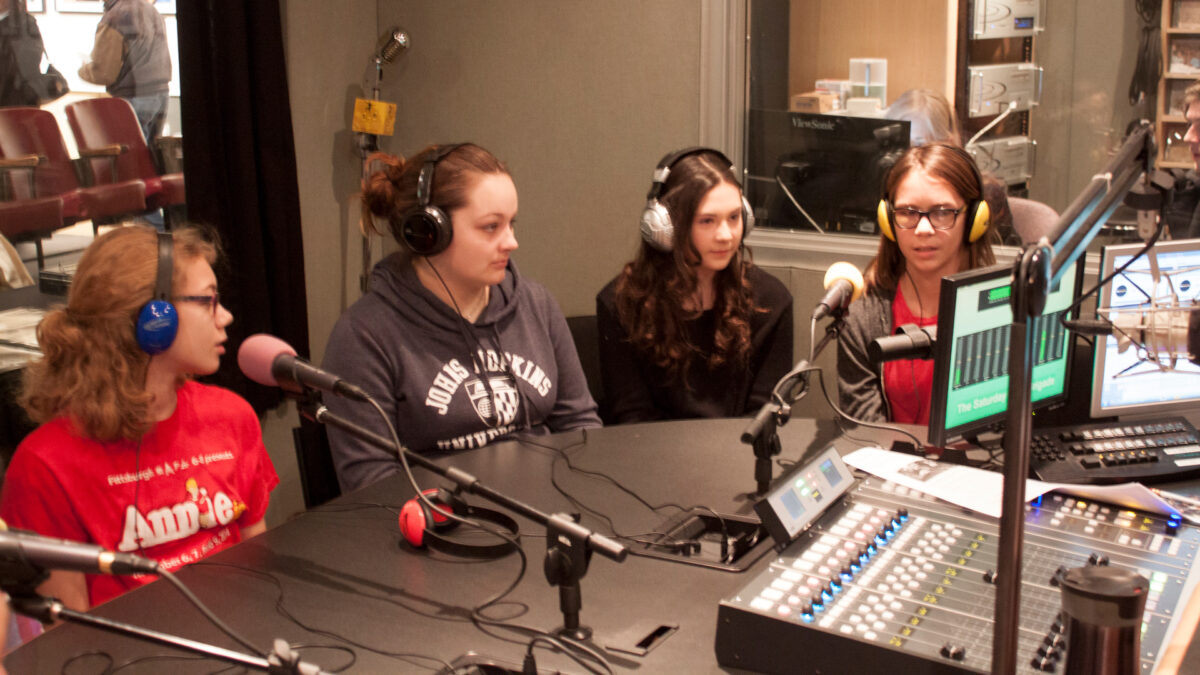 Four youth wearing headphones speaking into microphones in a radio studio